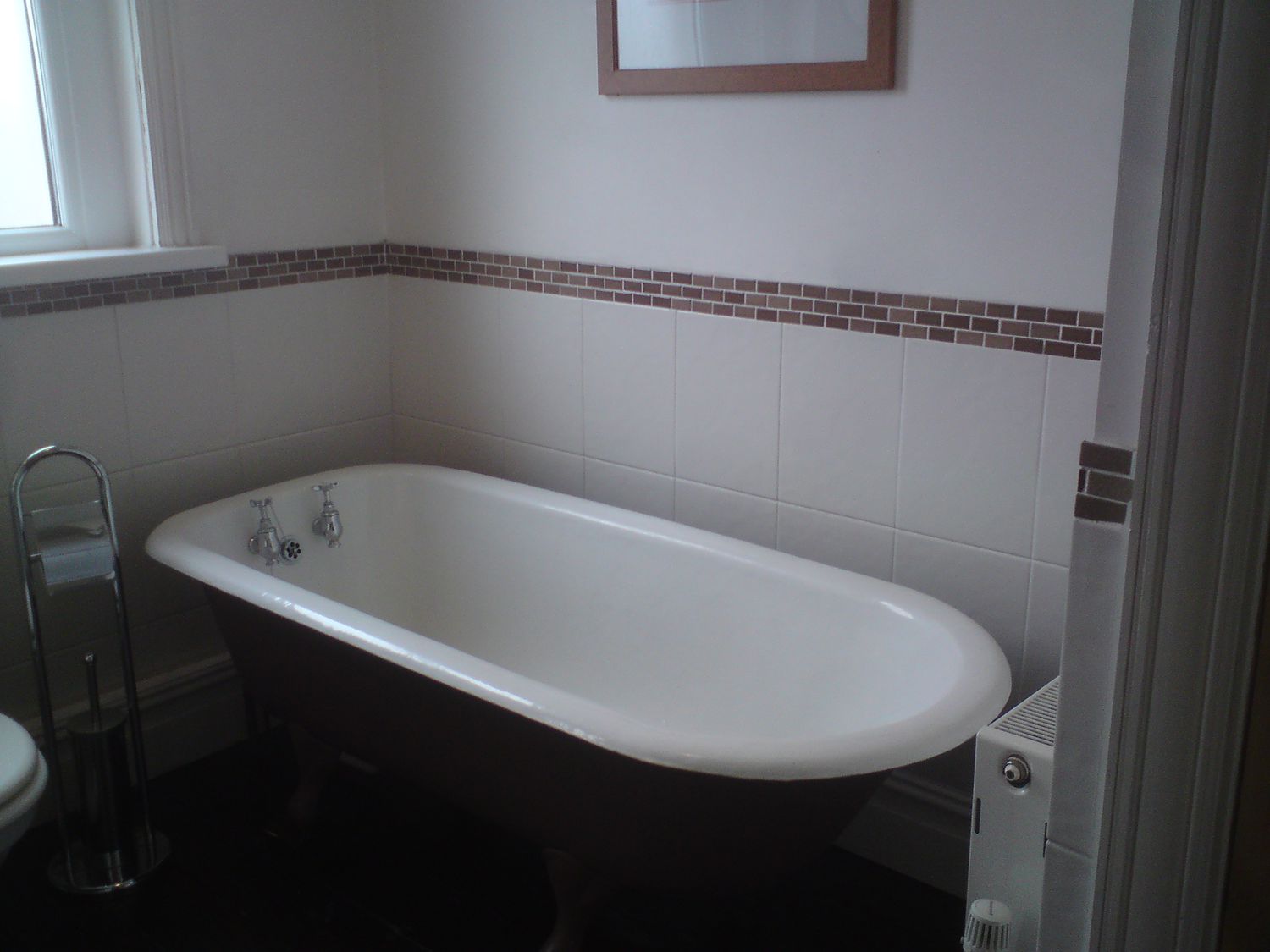 The same view of the old brown painted bath with grey tiles and brown mosaic tiles behind.