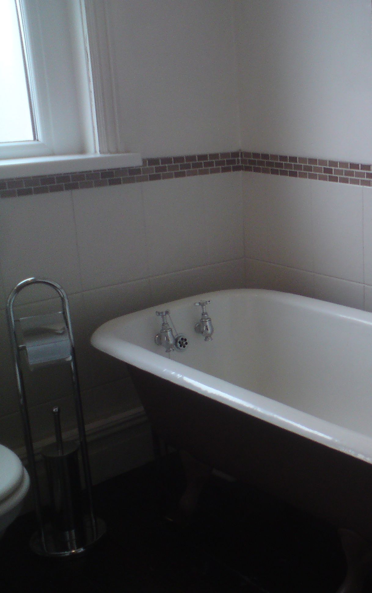 The old bath with grey tiles and a bare wall above.