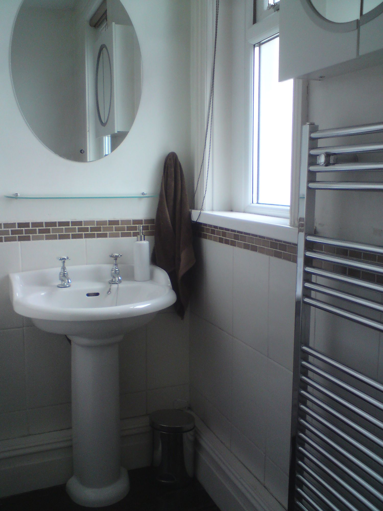 A photo of the old sink area which had a single pedestal sink with the chrome towel radiator to the side.