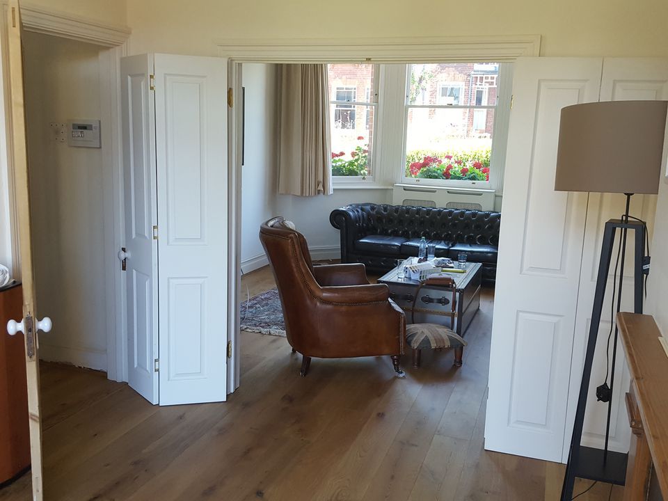 A view through the arch of the adjoining room to the cream painted room with a brown leather sofa.