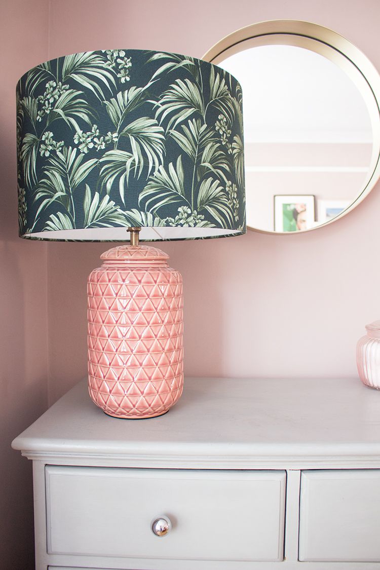 A close up of the new pink textured lamp with a green palm print lampshade on top of the grey chest of drawers.