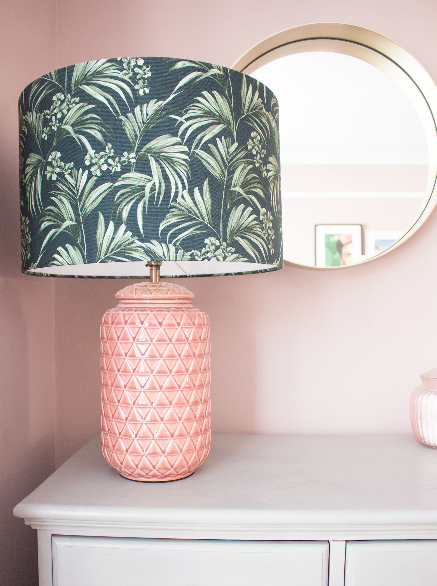 A close up of the new pink textured lamp with a green palm print lampshade on top of the grey chest of drawers.