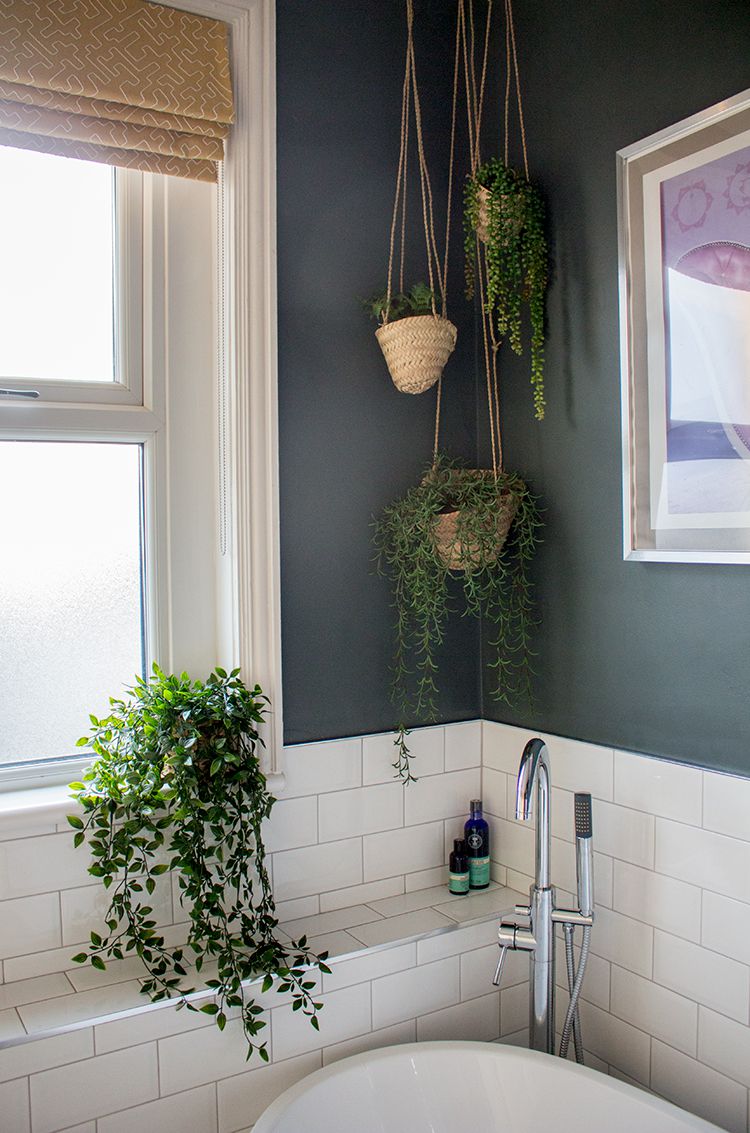 A photo of the corner above the bath, showing the hanging planters, the plant on the window sill, and the mustard yellow blind at the window.