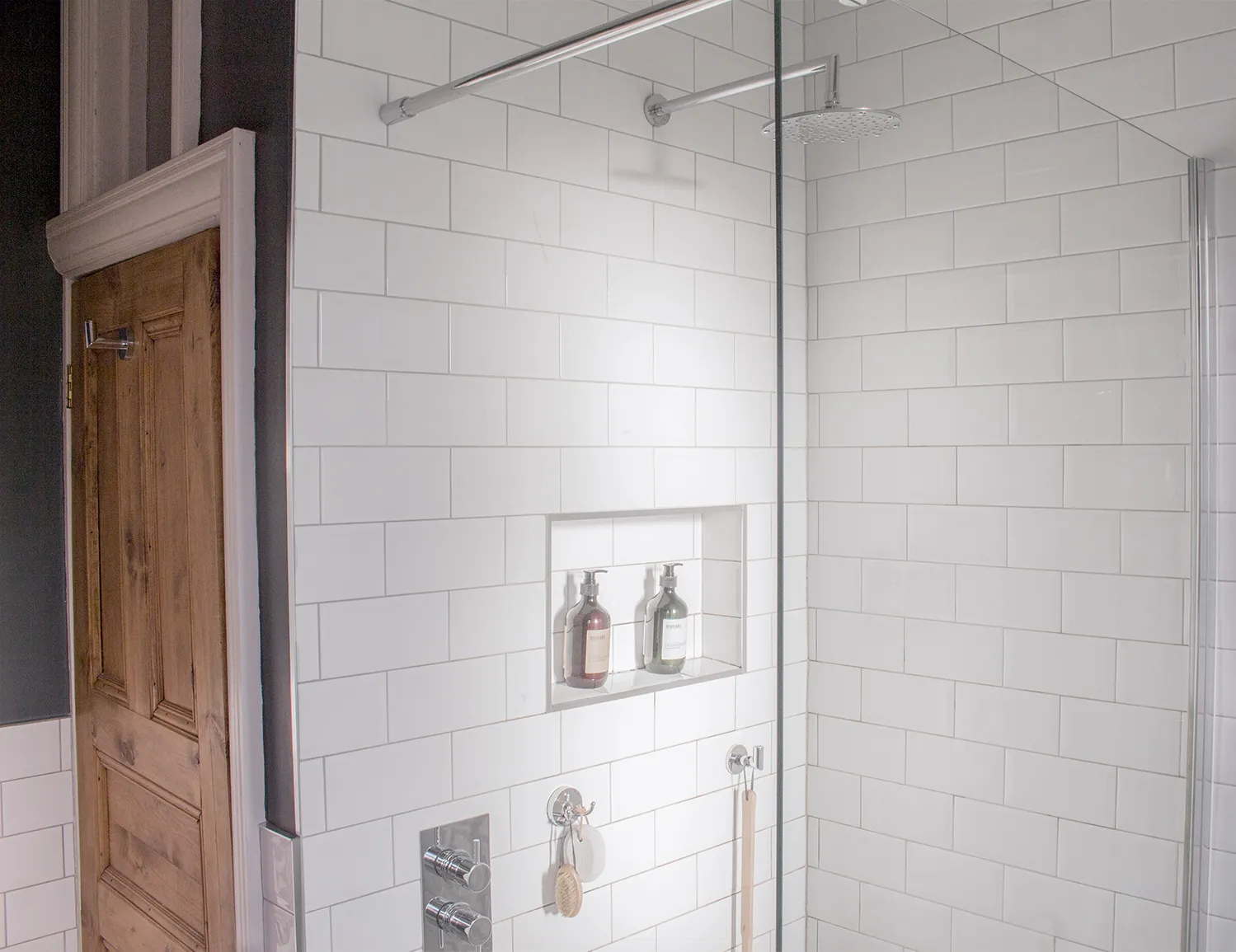 A photo of the new open shower area with one panel screen and a niche for toiletries.