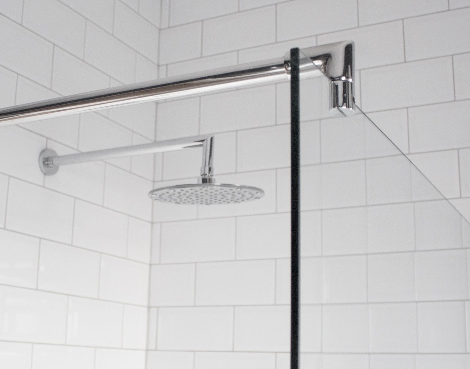 A close up of the new shower screen with the chrome shower head and metro tiles behind.