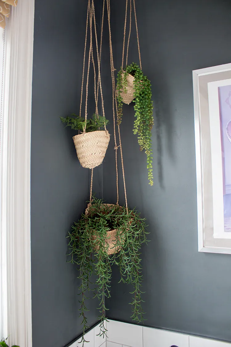 A close up photo of the three woven hanging planters with plants in them, hanging in the corner of the bathroom.