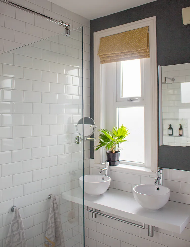 A photo of the new shower screen with the new double sinks behind, with new yellow blinds at the windows.