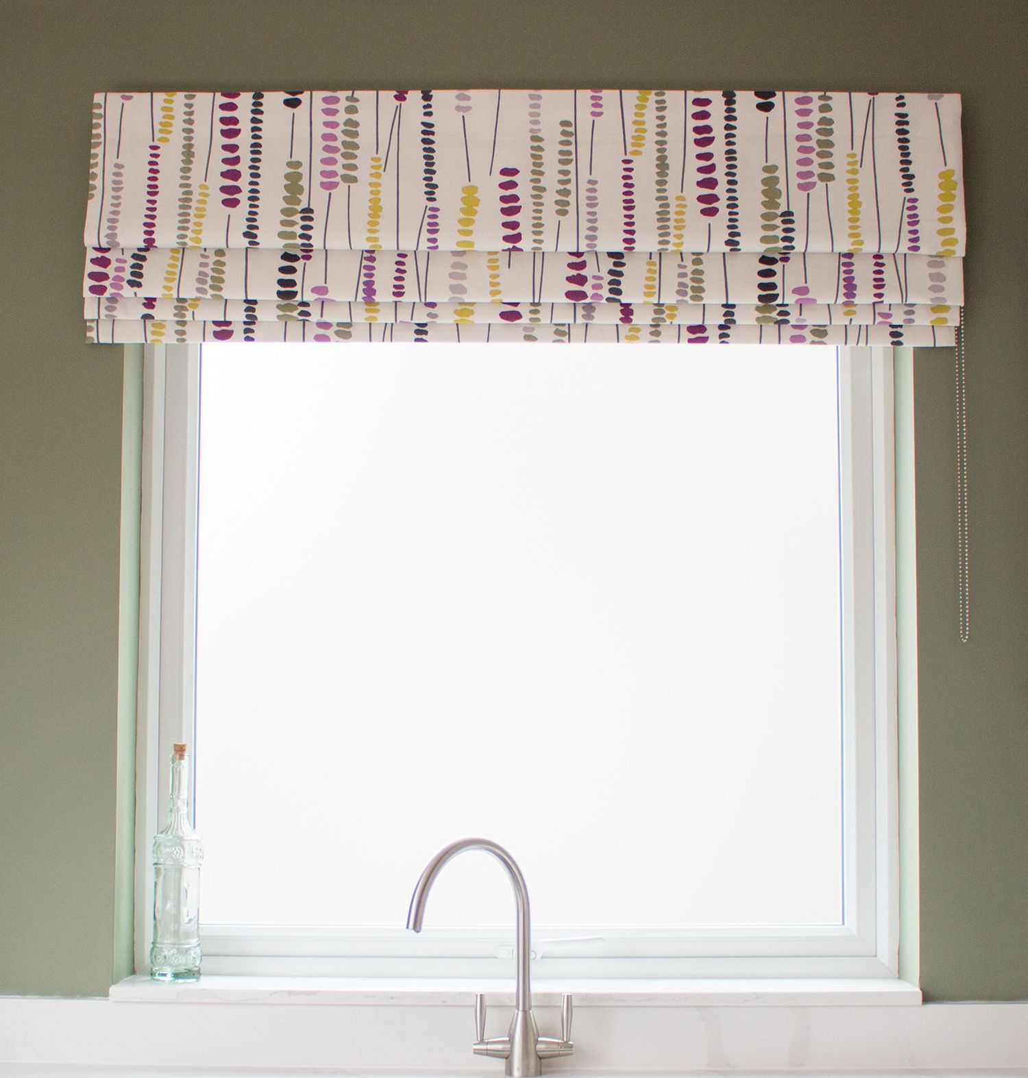 A photo showing the kitchen window with the green painted wall around it, and the new colourful Roman blind.