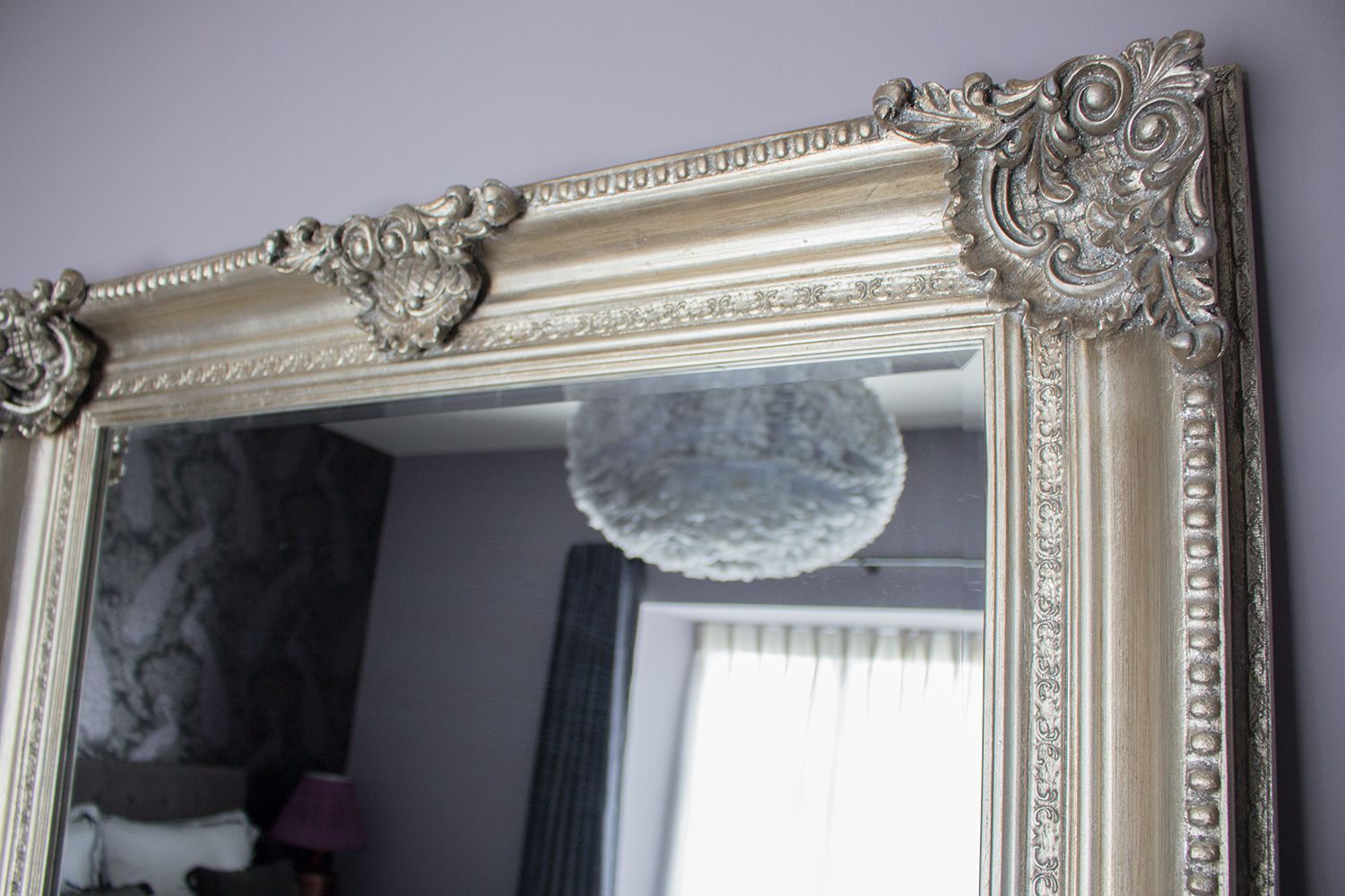 A close up of the corner of the floor mirror, with the rest of the room reflected in it.