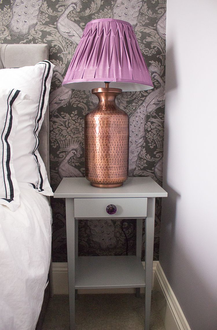 A photo of the new grey bedside table with a large copper lamp and purple pleated shade.