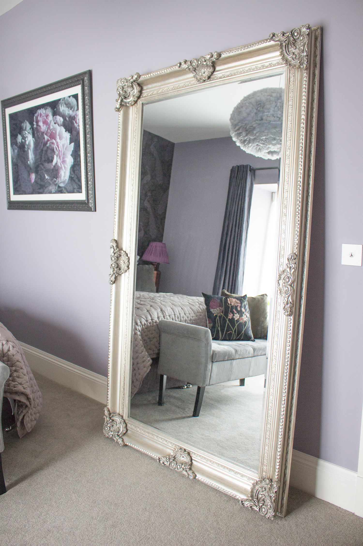 A photo of the large ornate silver floor standing mirror against the lilac walls.