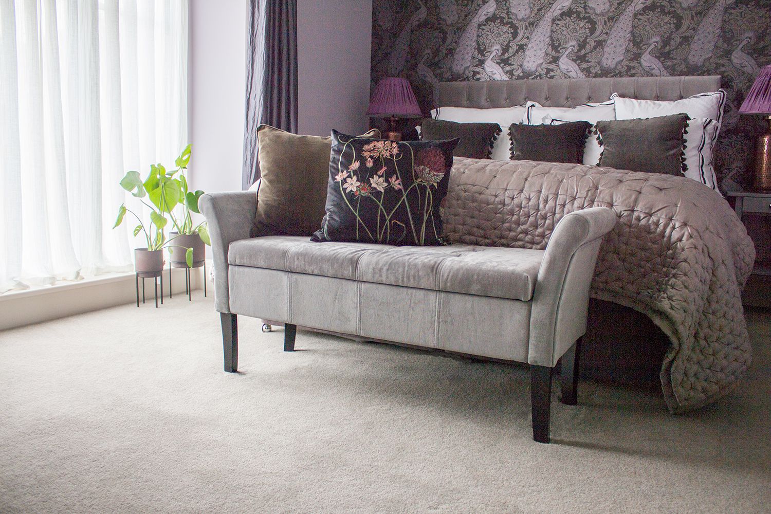 A view of the bed with the silk bedspread, and the grey velvet upholstered bench in front.