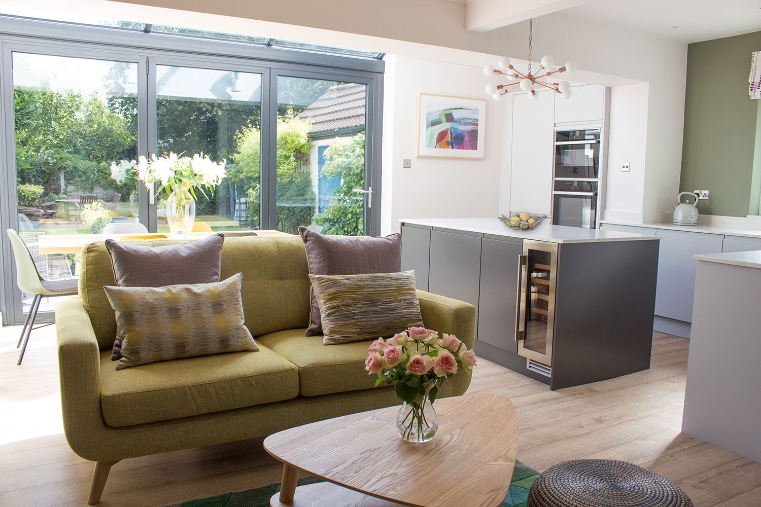 A photo of the pale green sofa, oak coffee table and the kitchen area and dining table behind.