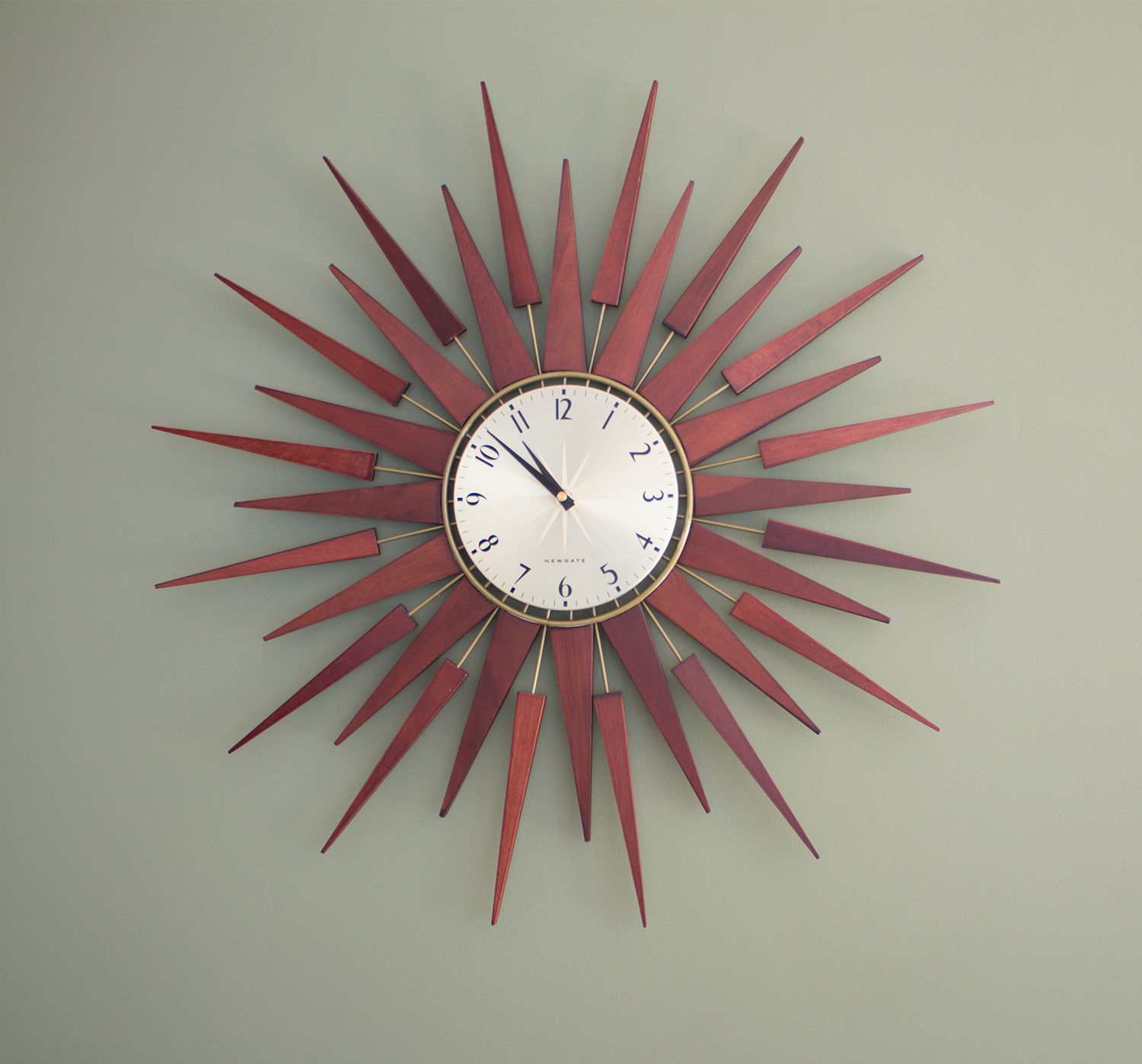 A close up of the walnut sunburst clock on the wall.