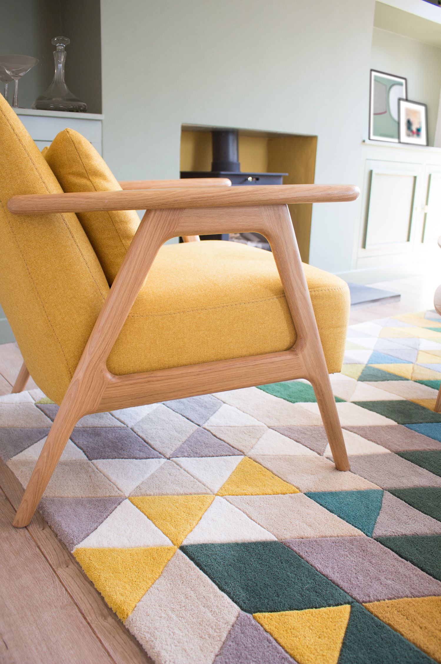 A photo of the yellow armchair with the colourful rug and the built in shelves and wood burning stove in the background.