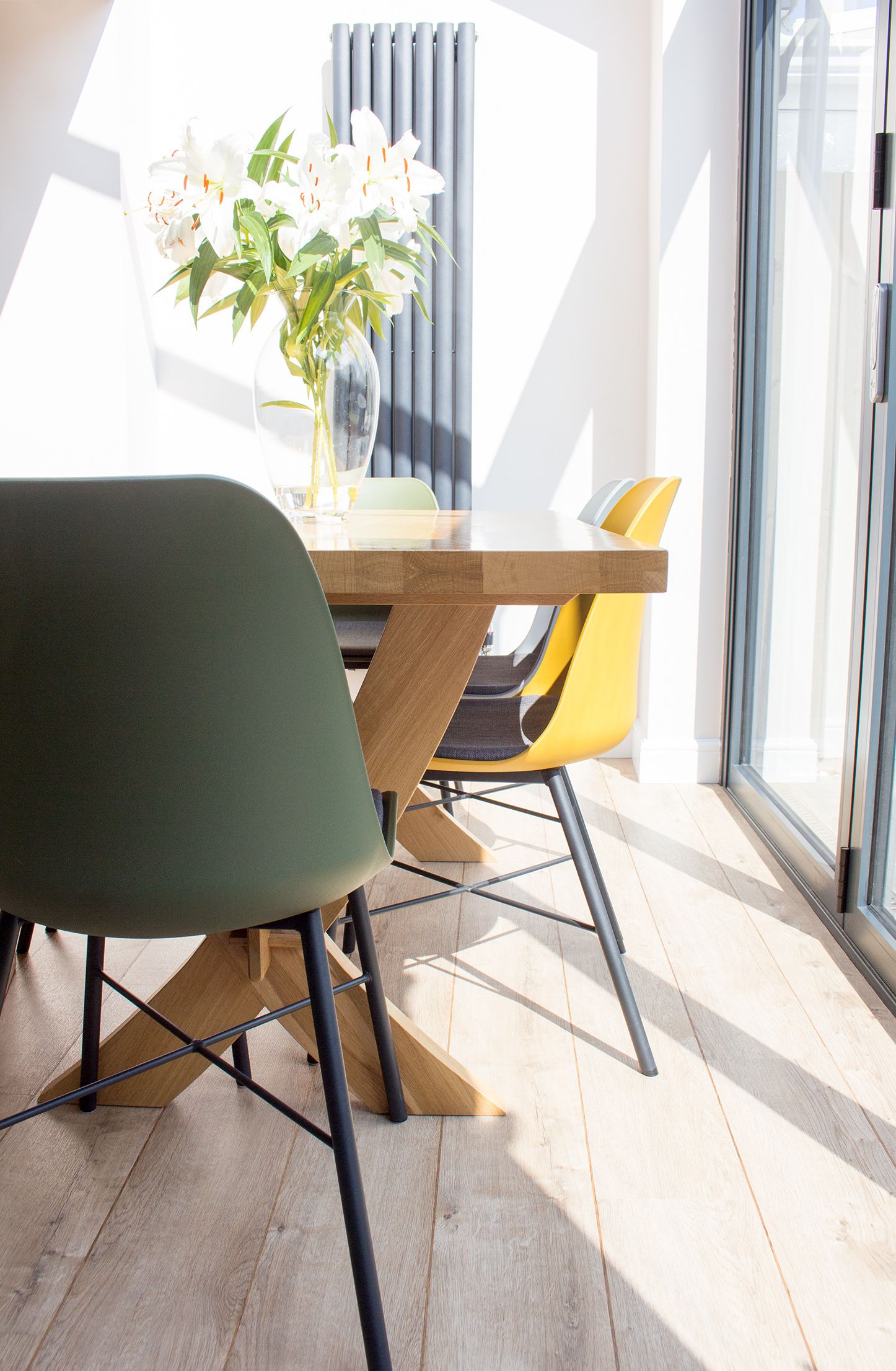 A photo of the new light oak flooring, the dining table and the yellow, green and grey dining chairs.