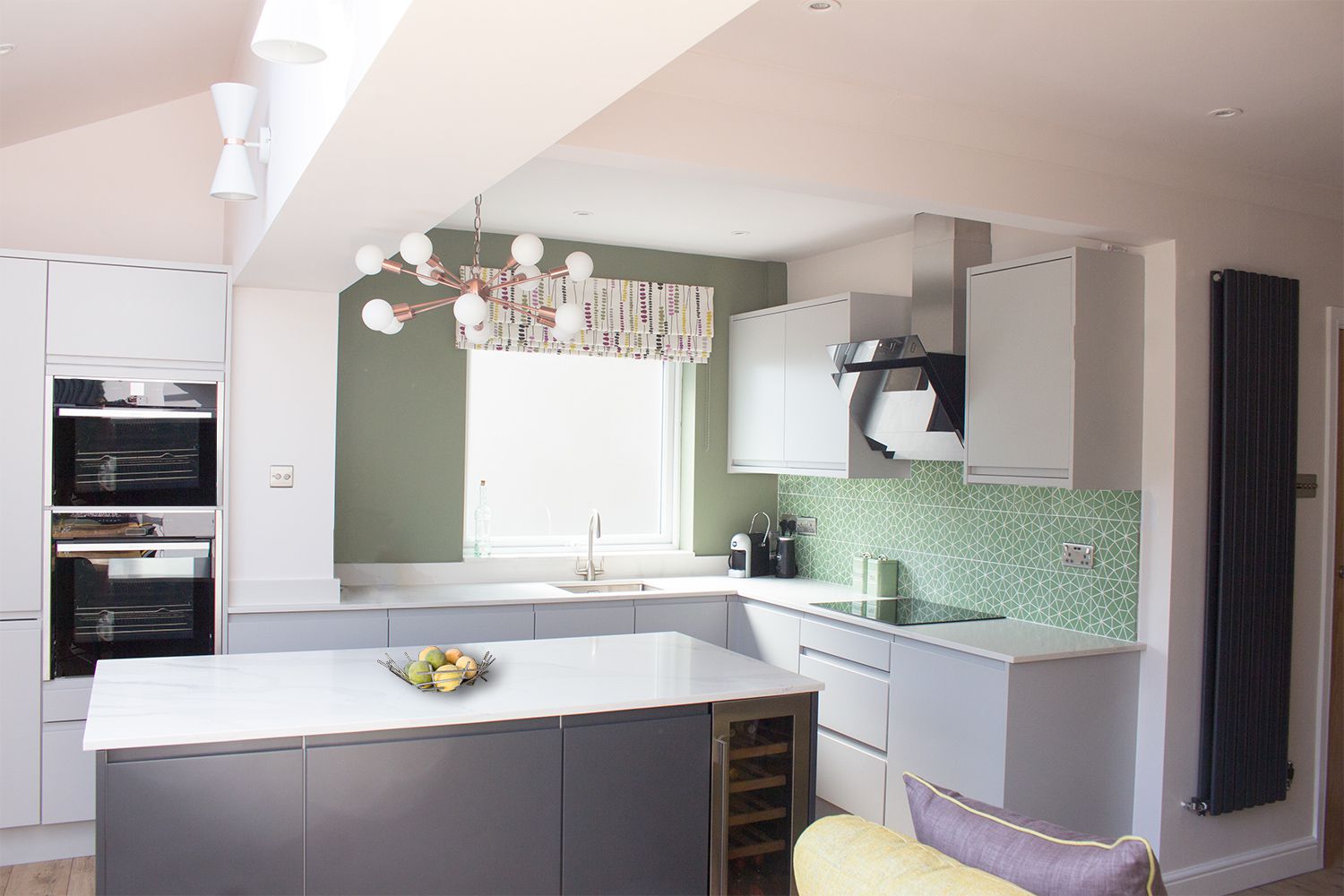 A photo of the kitchen area with light grey cabinets, marble worktops and a funky green geometric tile for the splashback.