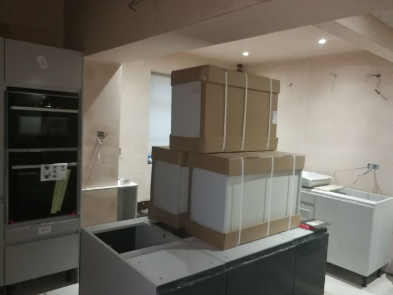 A photo of the same angle of the kitchen area with the units partially installed and bare plaster walls.