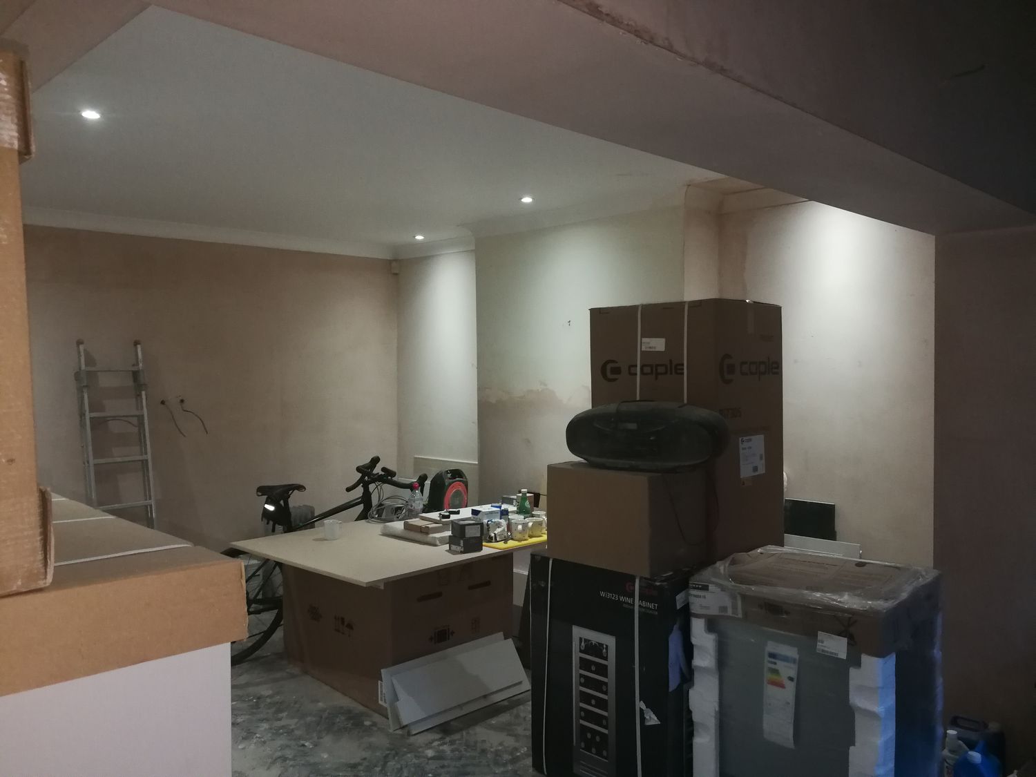 A photo of the same angle before the shelving was built, with bare plaster walls and some of the kitchen units stacked up.