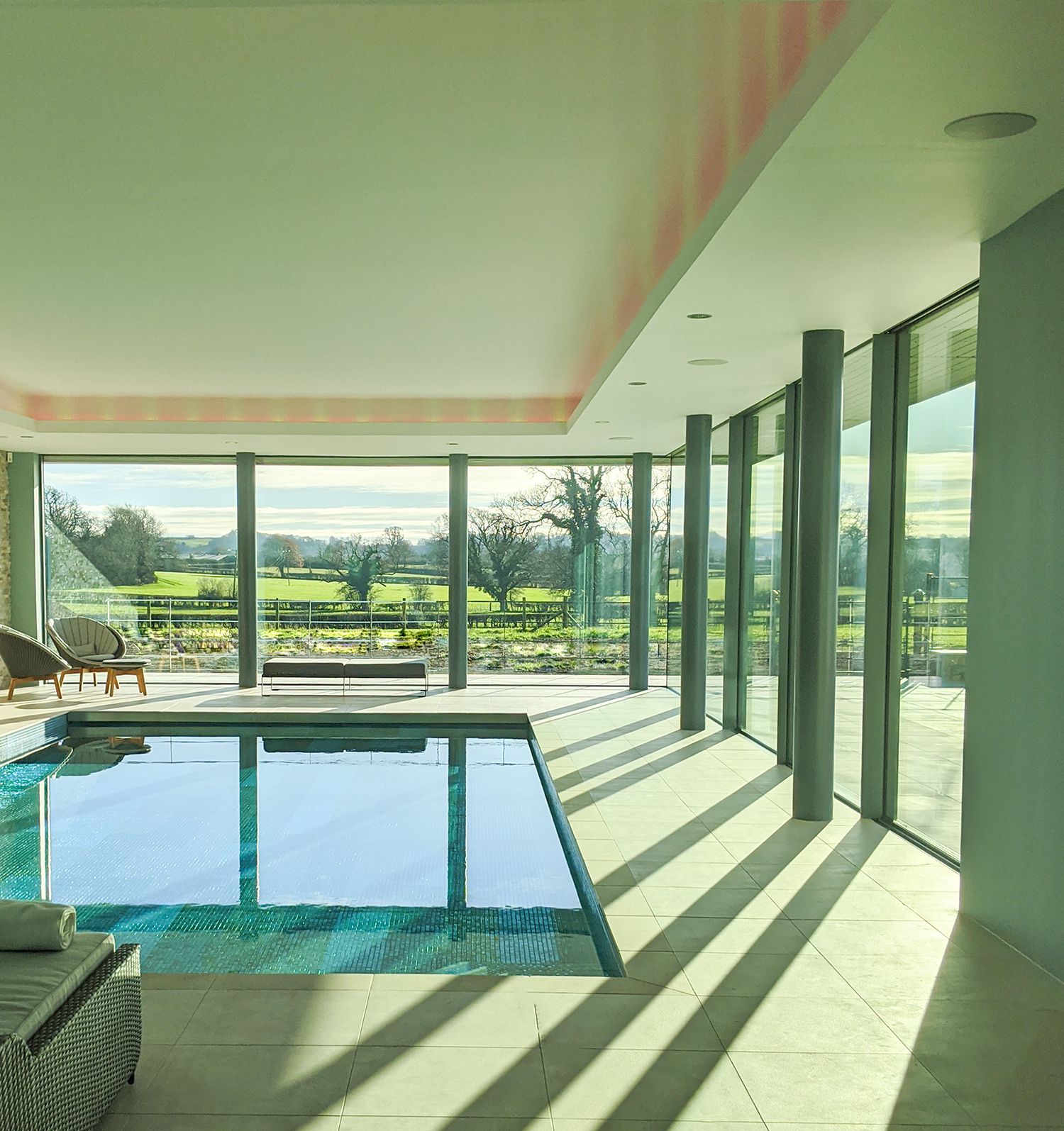 A photo looking down the length of the pool, with the sun streaming in through the glazing.