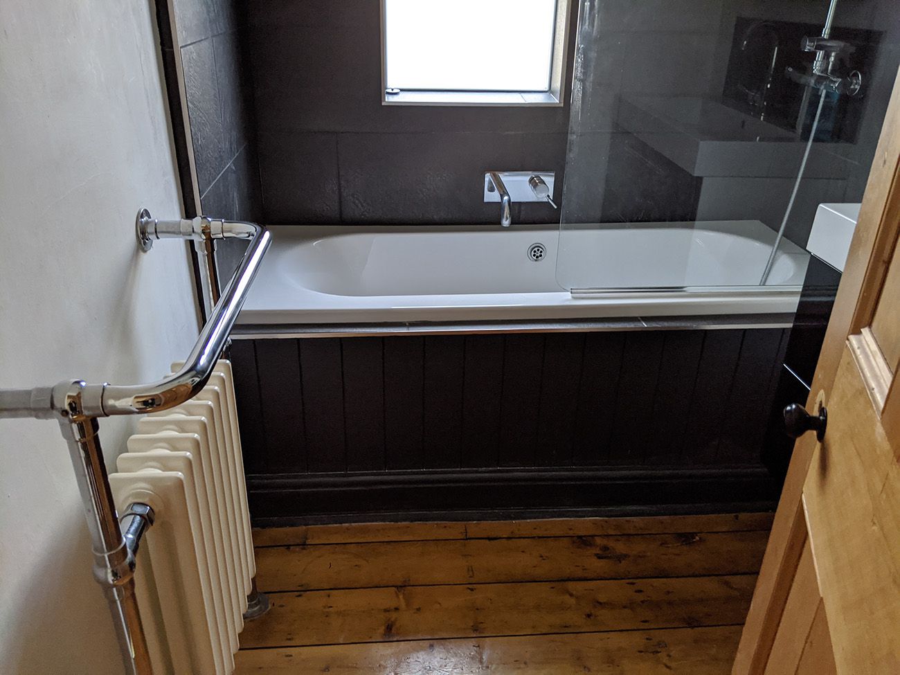 The bathroom was dark grey with chrome fittings and wooden floorboards before the redesign.