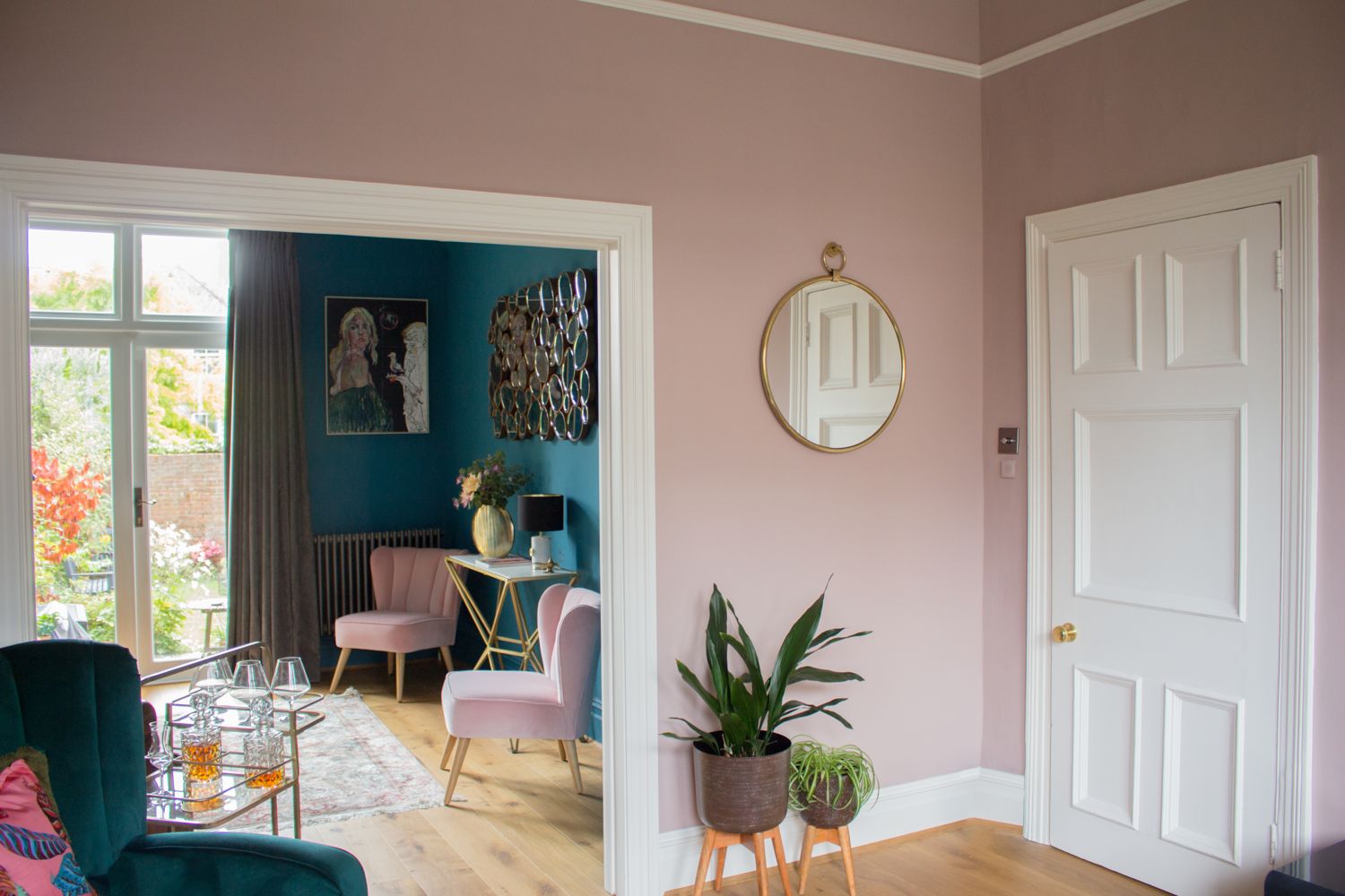 A photo of the knocked through reception rooms, one is painted teal and the other is painted pink, with sumptuous velvet furniture.