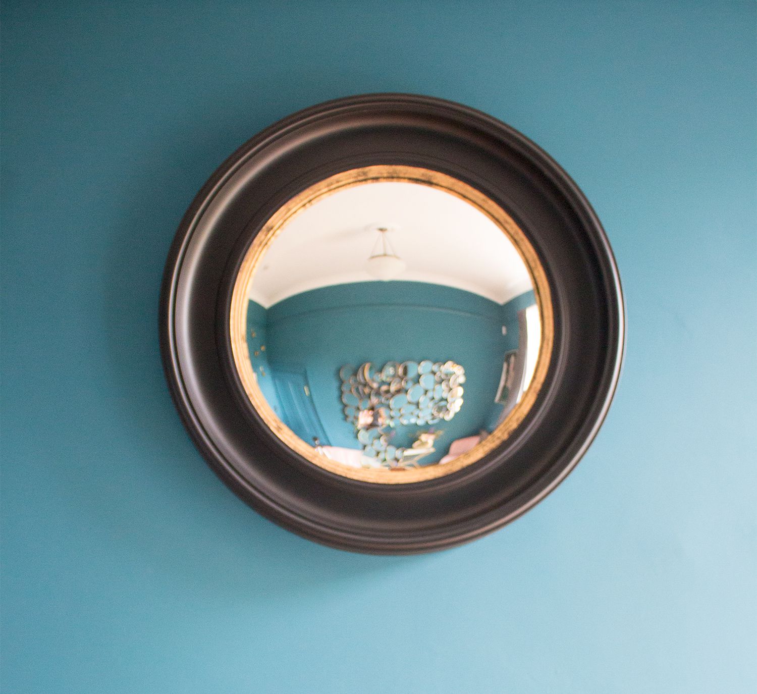 A close up photo of the black round mirror in the teal painted room.