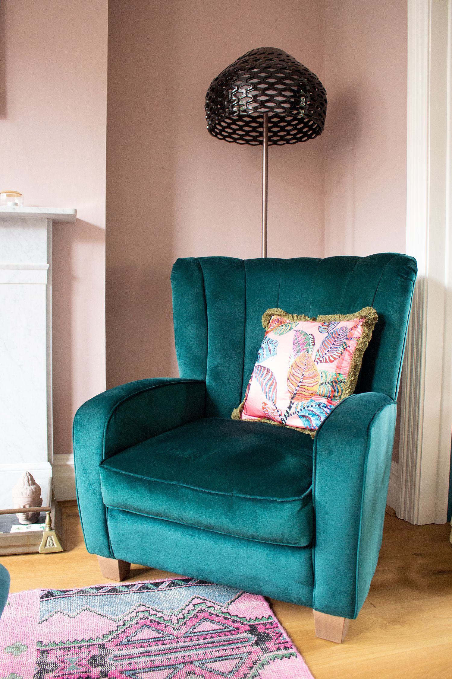 A teal velvet chair with a black standard lamp behind it.
