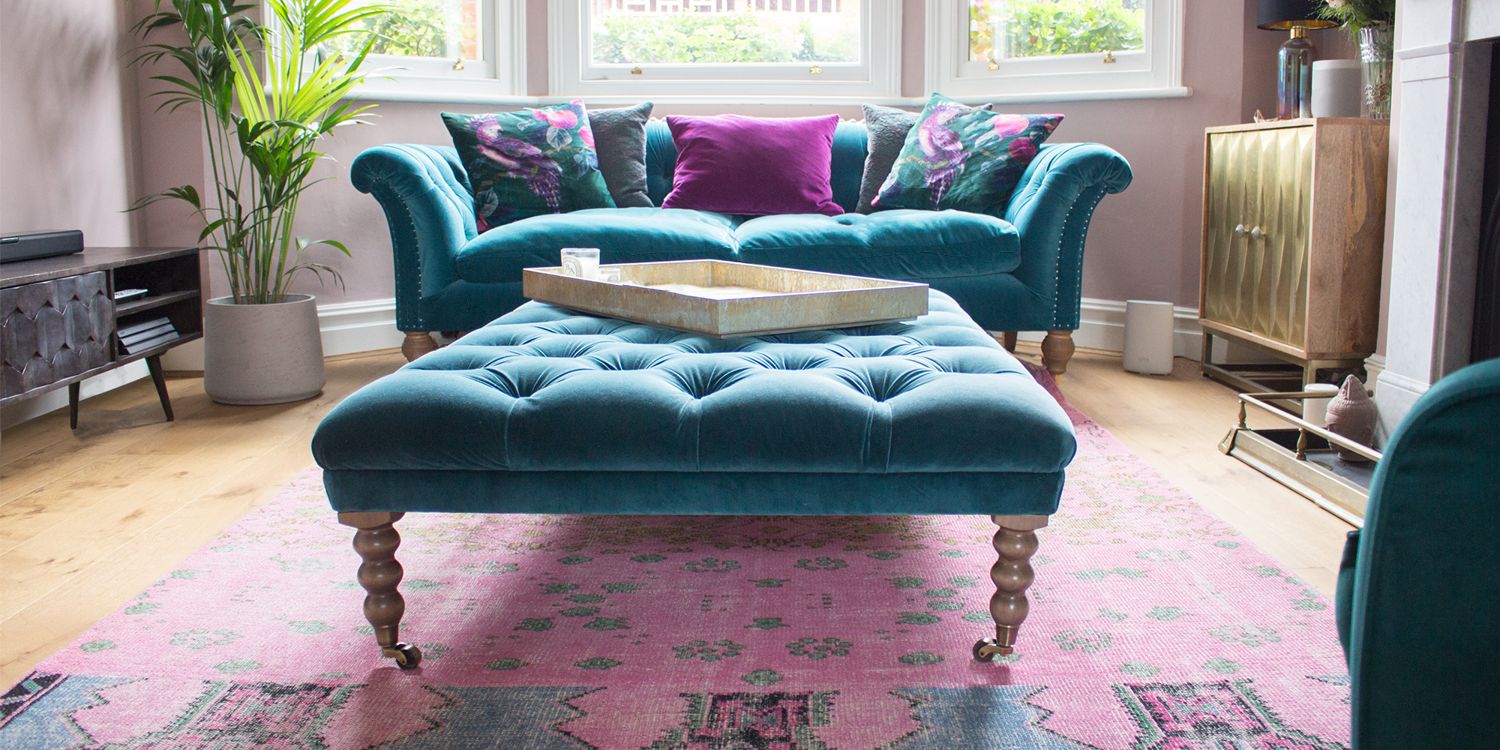 A close up of the teal velvet footstool in front of the teal velvet sofa.