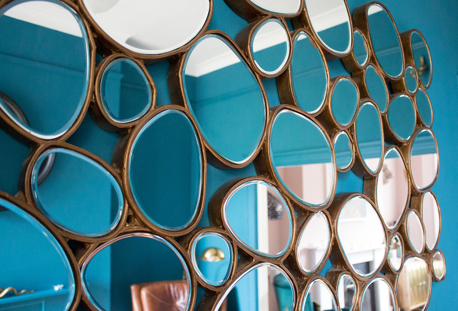 A close up photo of a brass mirror made up of circles in the teal room.