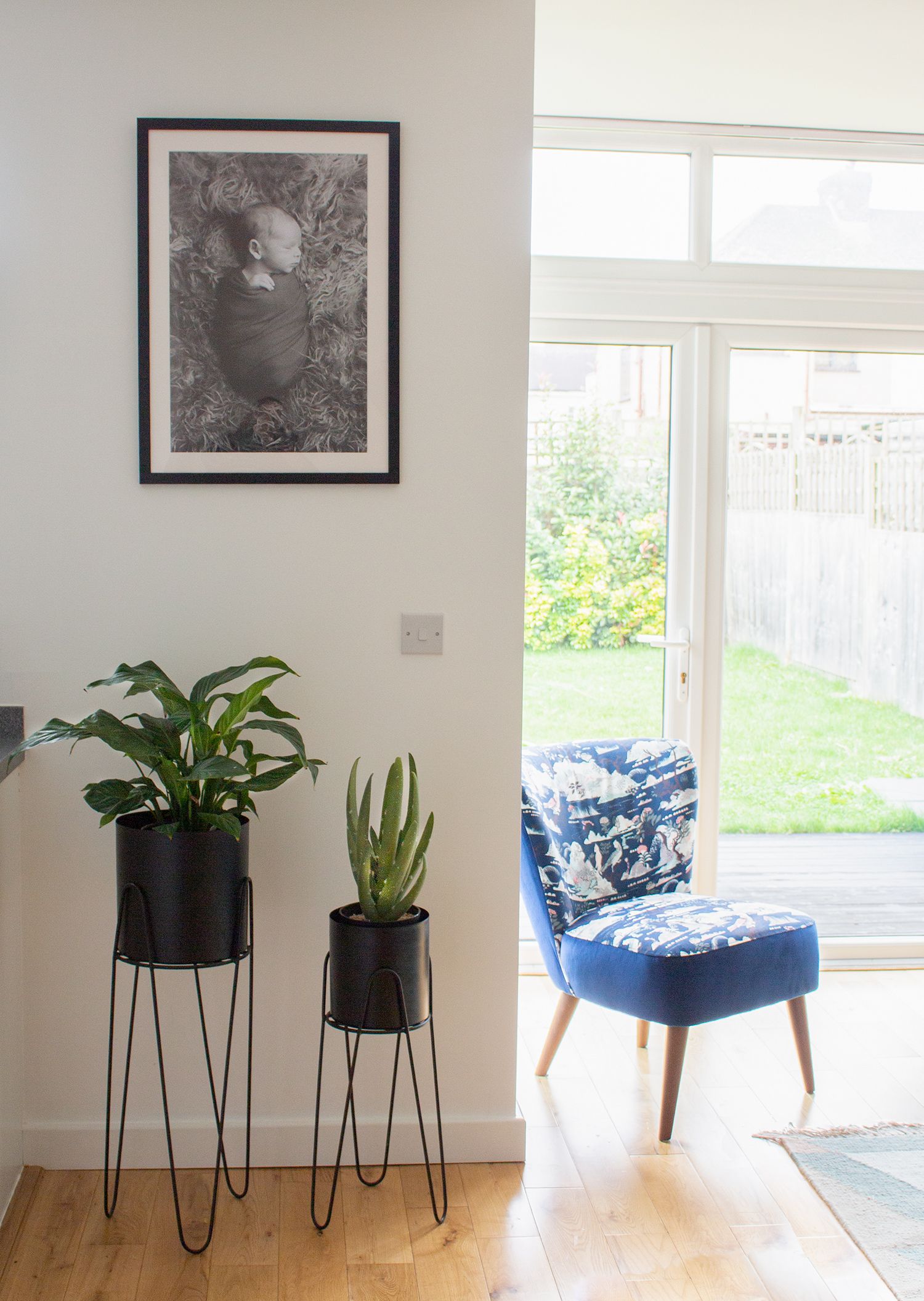 A photo of the chair by the windows, with two black planters and a personal photo on the wall.
