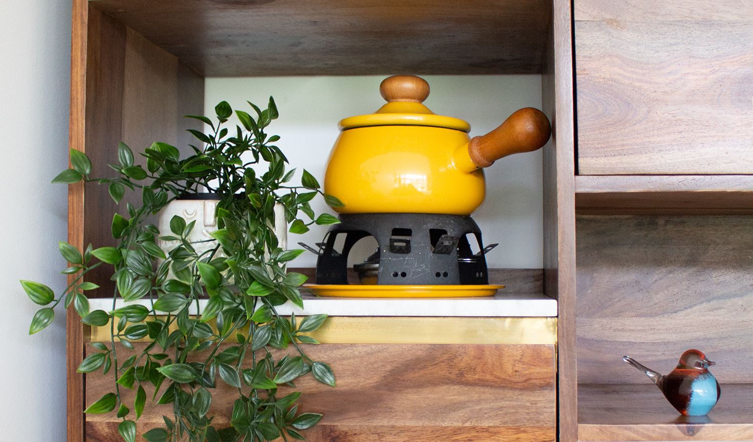 A close up of the walnut shelf unit, styled with plants and a yellow fondue set.