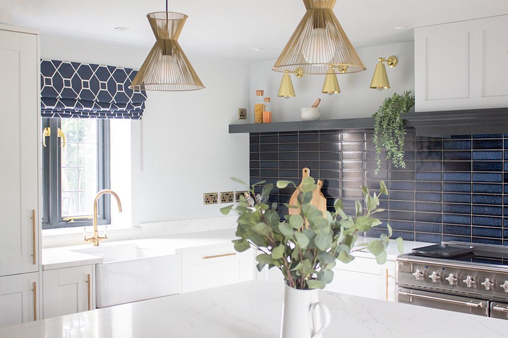A view of the kitchen with the white shaker style units, marble worktops and brass lighting.