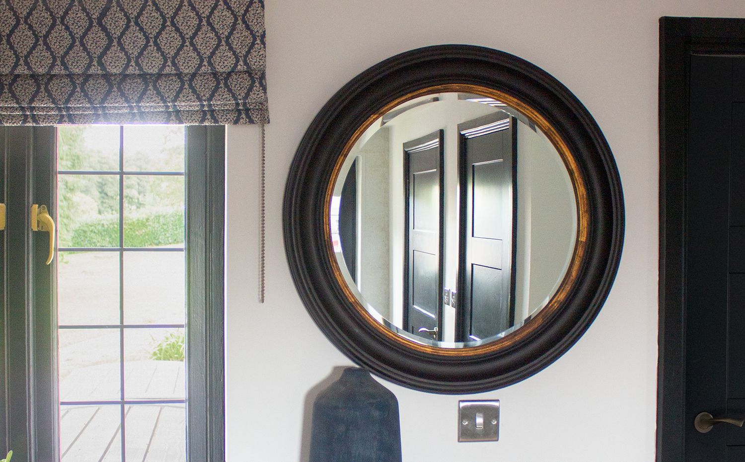 A close up of the black round mirror, with a reflection of the black doors in the hallway.