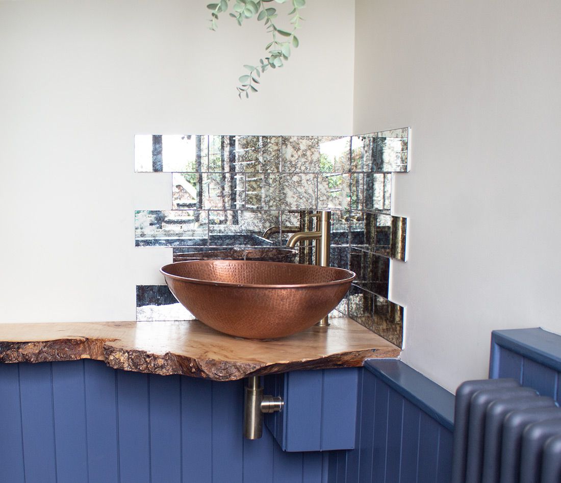 The new sink area with wooden shelf, countertop sink and foxed mirror tiles behind.