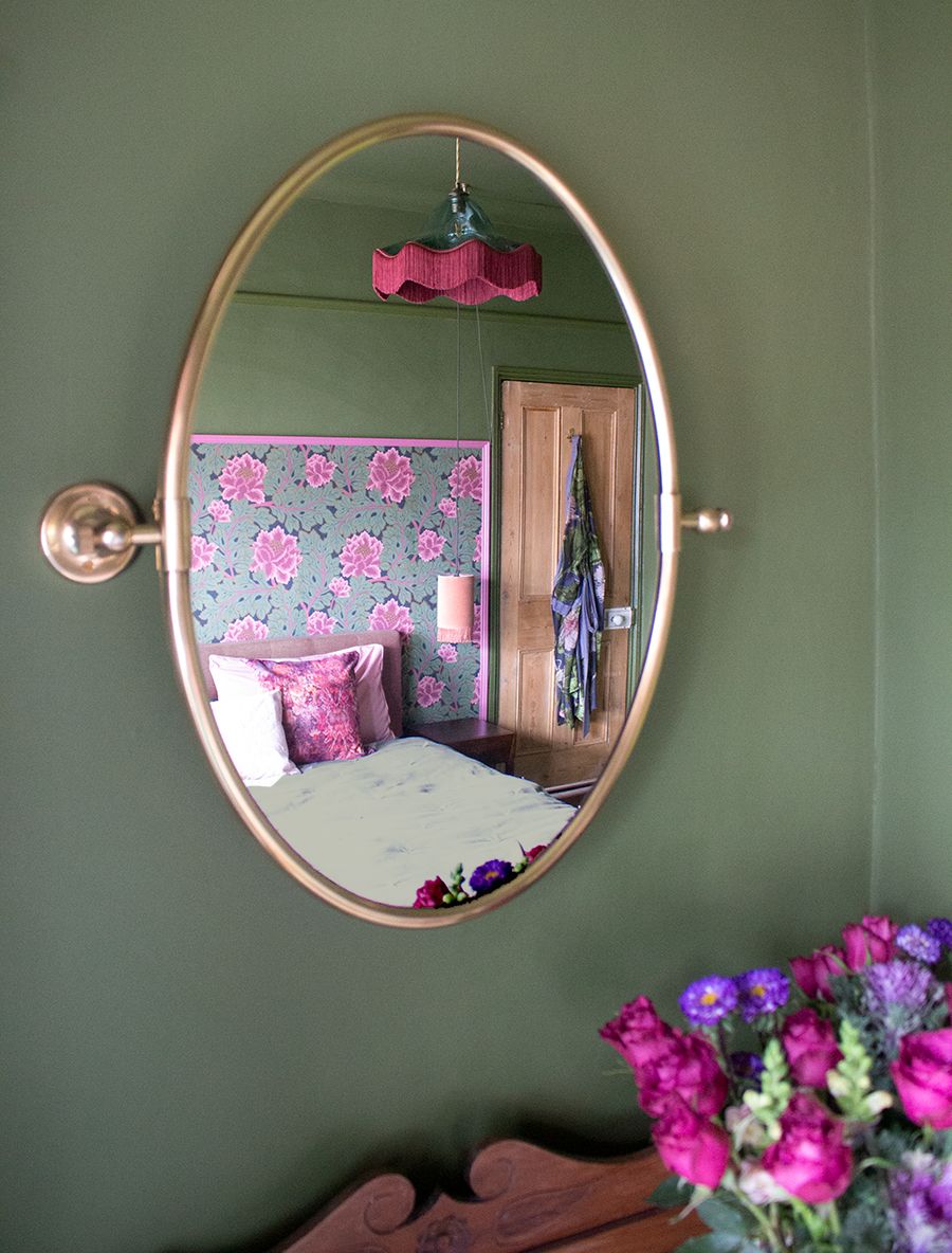 A close up of a brass oval mirror, with the main bedroom reflected in the glass.