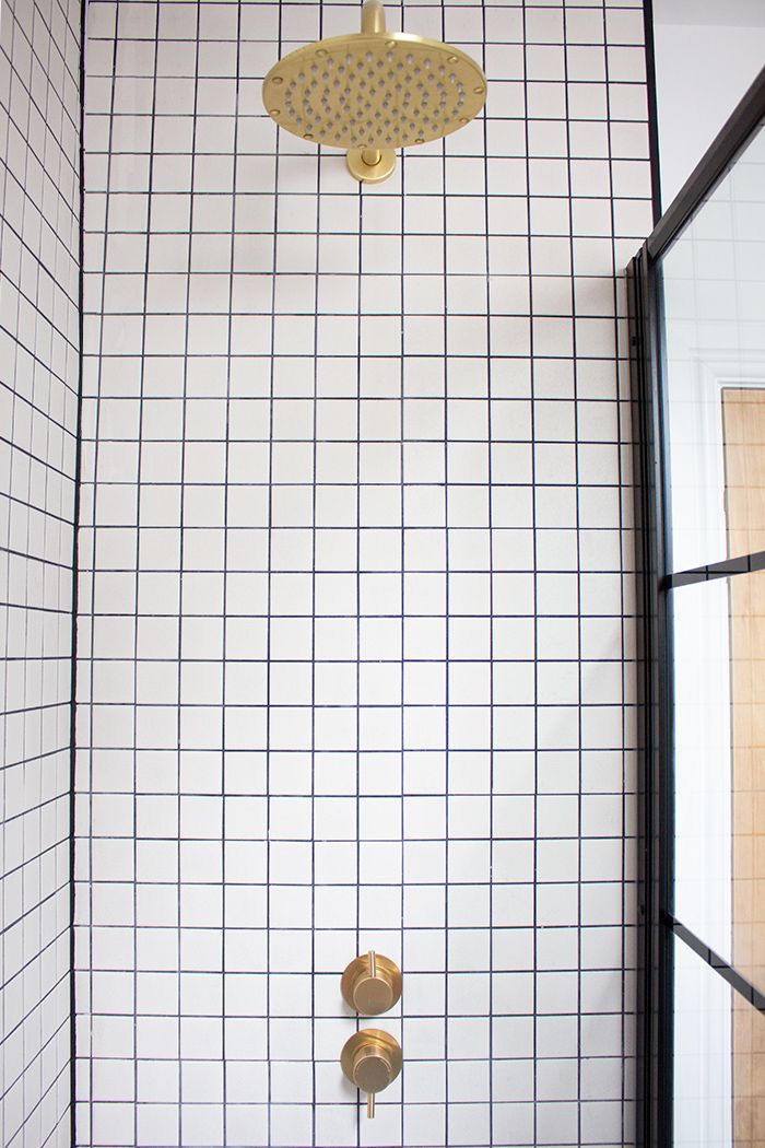 A photo of the new brass shower head and valve with the square grid tiles around them.