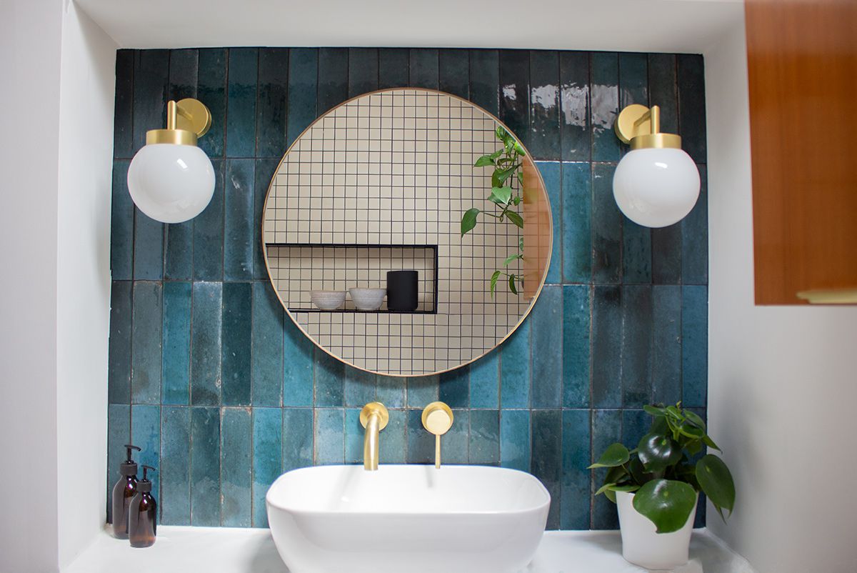 A view of the new sink with brass wall spout and globe lighting either side of a round mirror above.