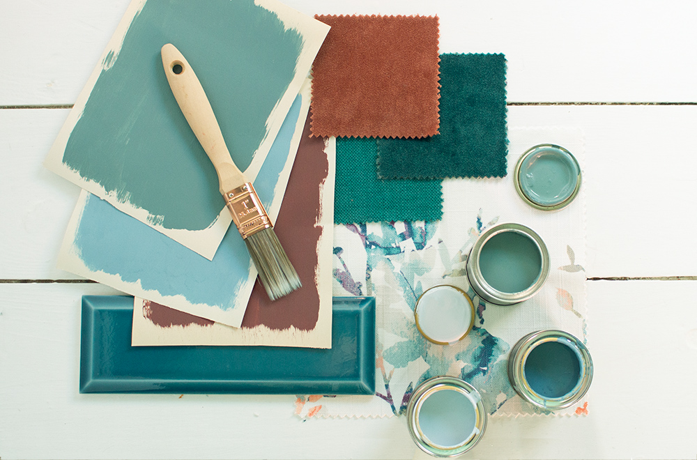 A photo of the Designer in a Box with some paint charts, open paint pots, a paint brush and some tiles placed around it.
