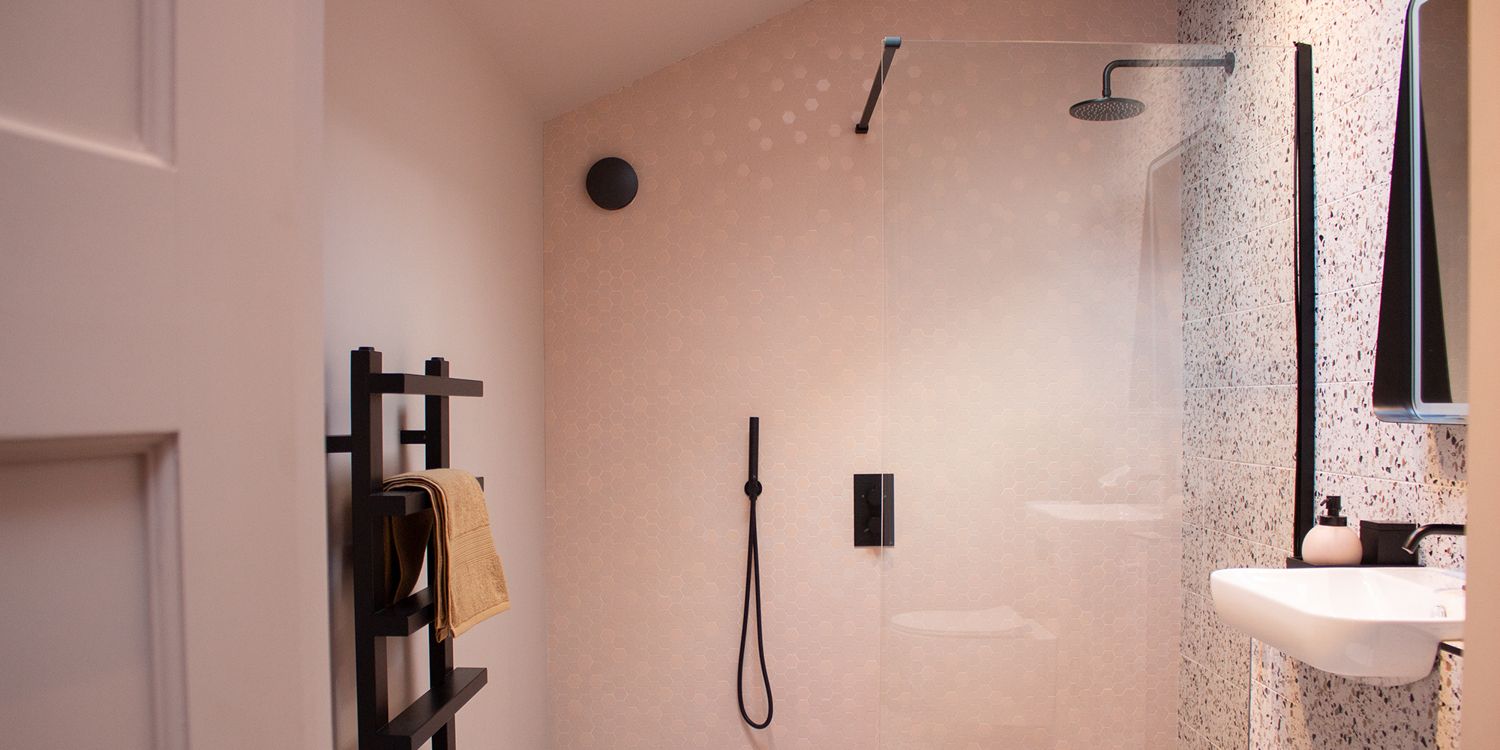 A photo of a bathroom tiled in pink hexagon tiles, with black shower and taps.
