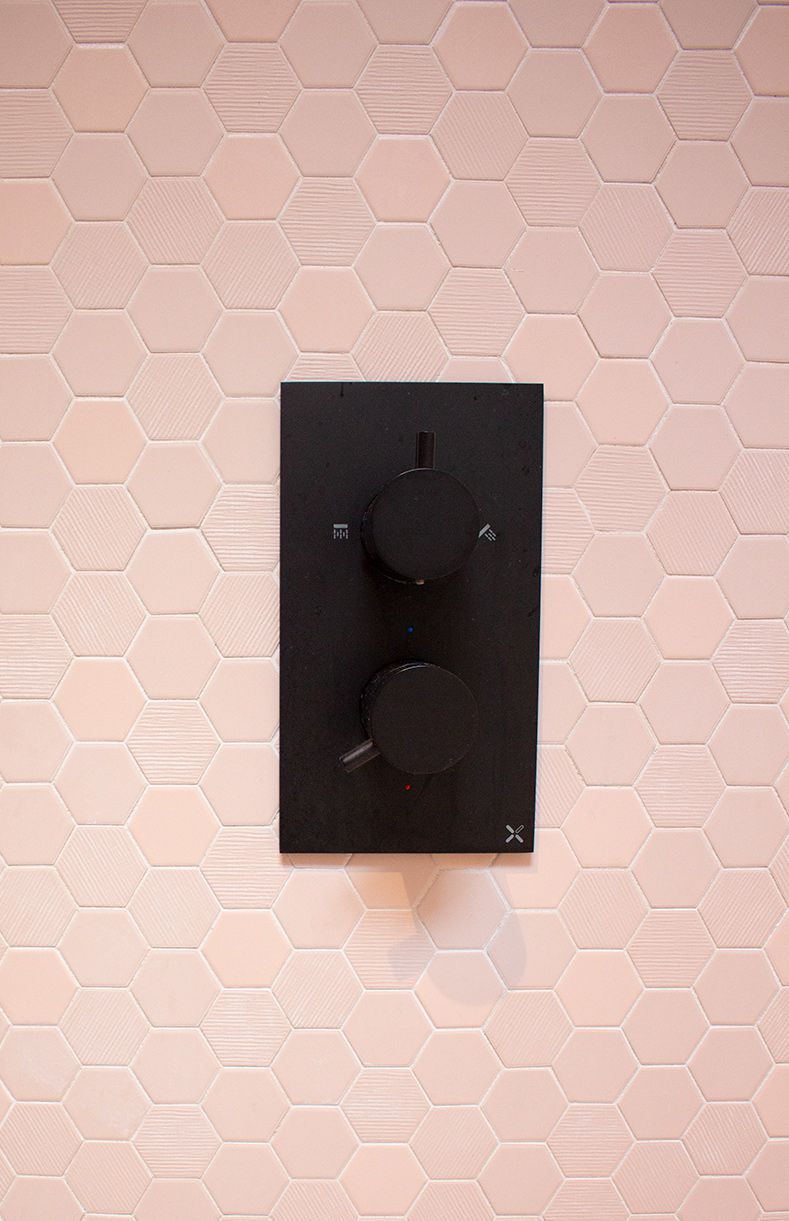 A close up of the black shower valve and the pink hexagonal tiles in the wet room.