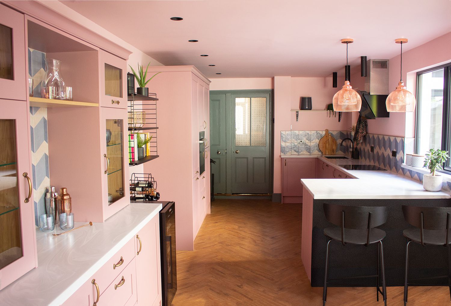 A photo of the pink and green kitchen, showing the bar stools and the view to the hallway.
