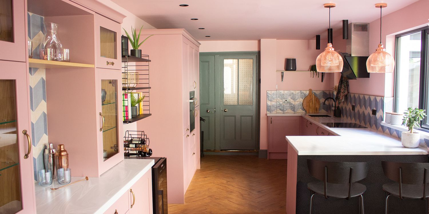 A photo of a kitchen with pink walls and units and green doors.