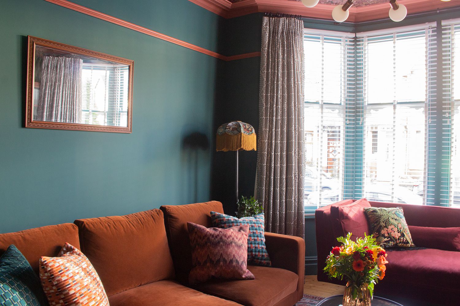 A photo showing the brown velvet sofa and the bay windows, with white Venetian blinds hung at them.