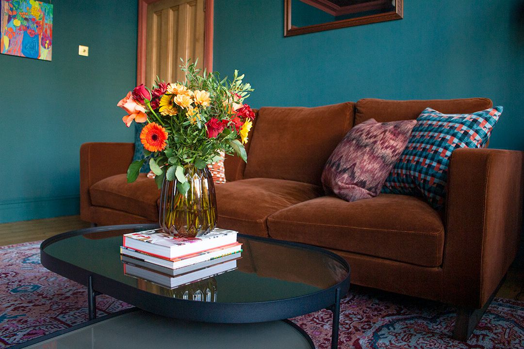 A photo showing the width of the velvet cocoa coloured sofa, with bright, fresh flowers on the coffee table in front.