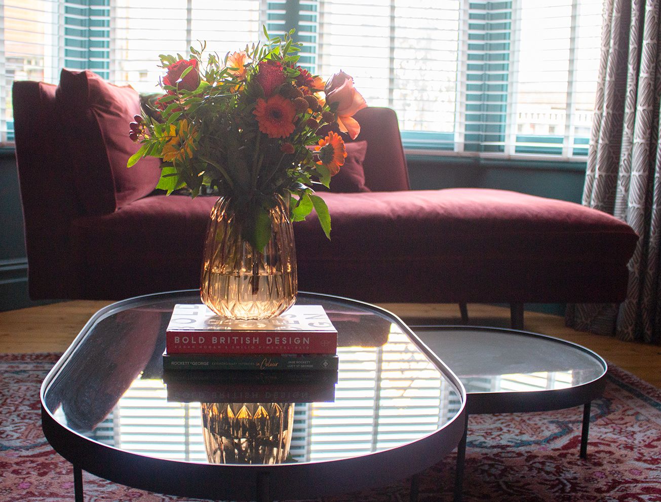A photo showing the claret coloured chaise long, with brightly coloured flowers in front of it on the coffee table.