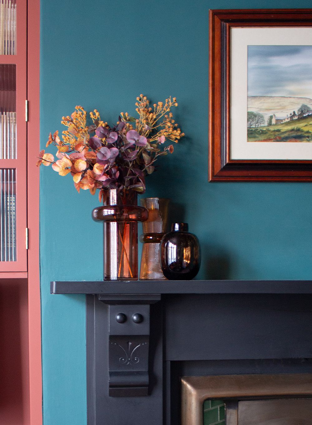 A close up of some orange and purple flowers and foliage on a black mantlepiece.