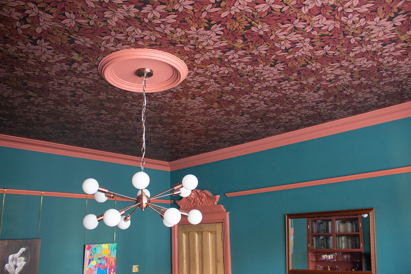 A photo showing the wallpapered ceiling with ceiling light, and the elaborate architrave around the door in the background.