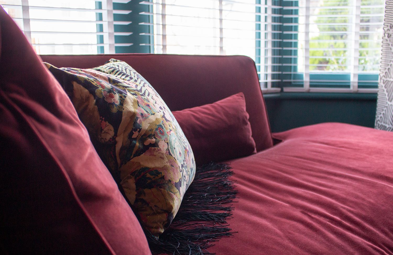 A close up of the brightly coloured and patterned cushion on the claret coloured velvet chaise.