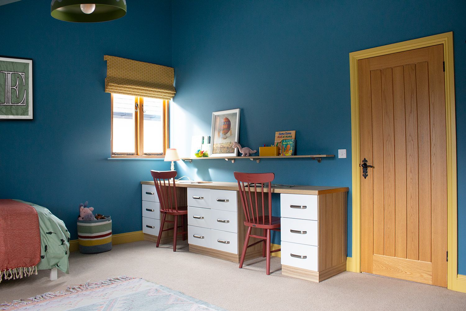 A photo of a child's bedroom showing the desk area with two burgundy chairs against blue walls with yellow accents,